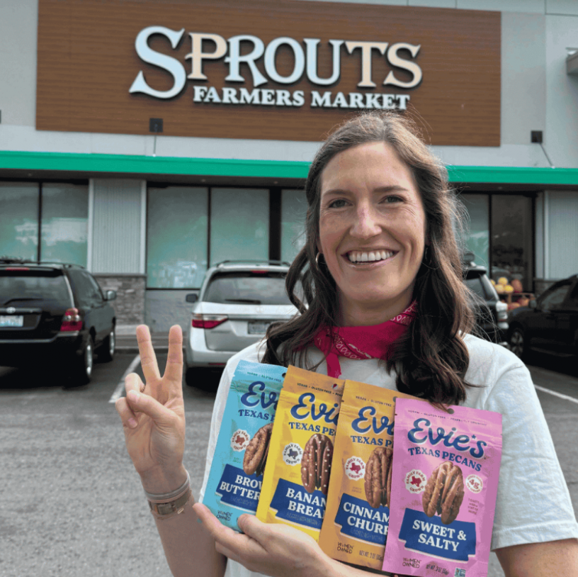 Co-Founder Evie in front of Sprouts holding all four flavors of Evie's Snacks. 